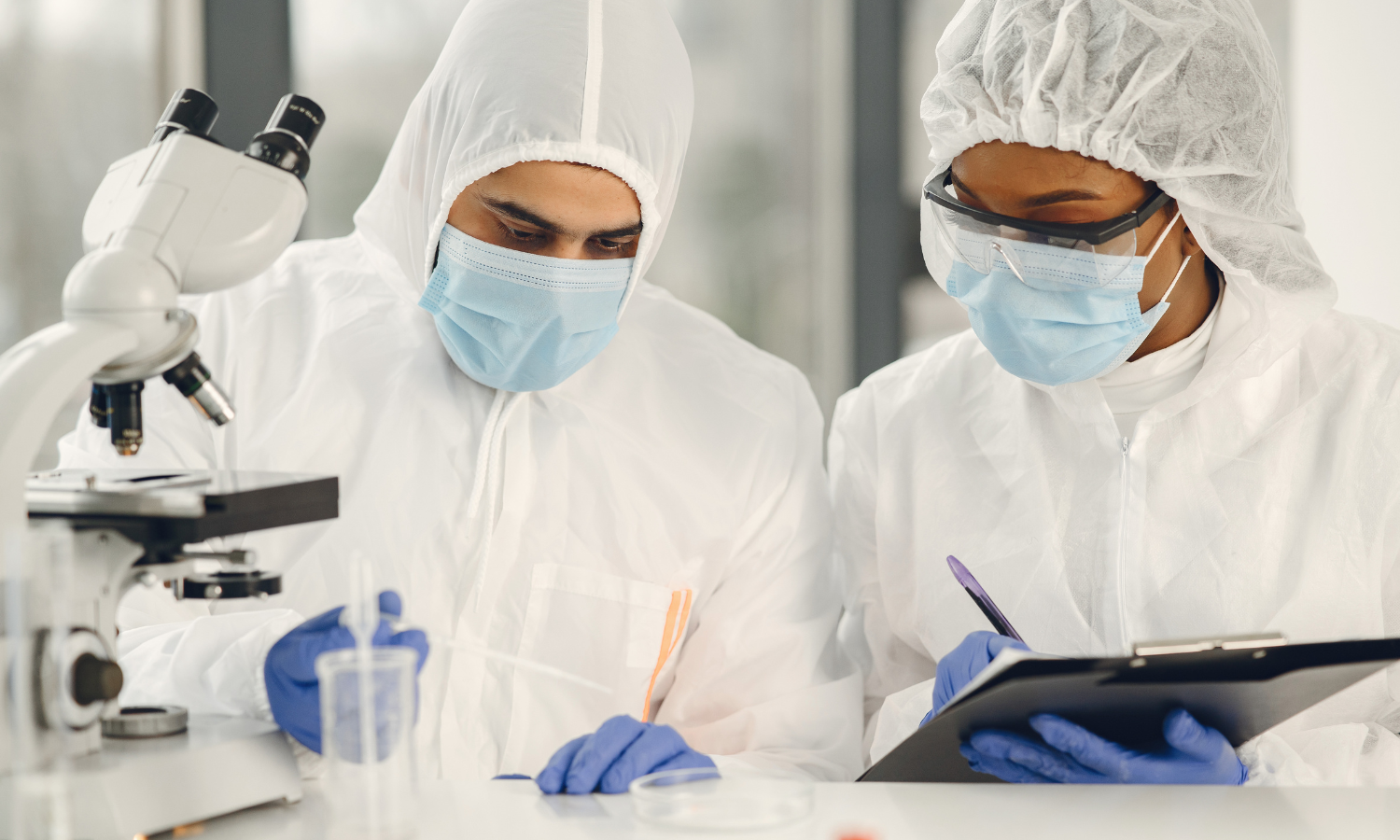 Profissionais em laboratório realizam análises técnicas com microscópio, seguindo protocolos de segurança, controle de qualidade e conformidade regulatória